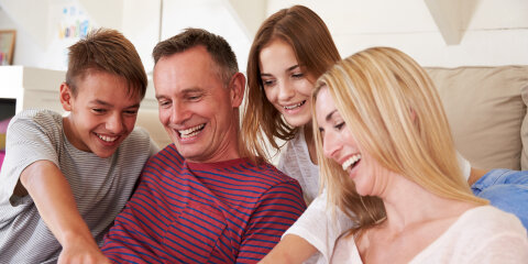 Family With Teenage Children Sitting On Sofa Looking At Mobile Phone At Home