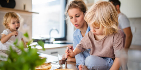 Young family with two small children indoors in kitchen, eating pancakes.