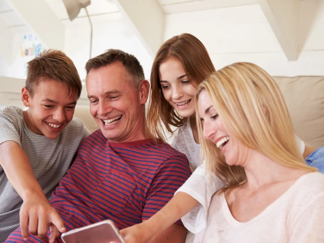 Family With Teenage Children Sitting On Sofa Looking At Mobile Phone At Home