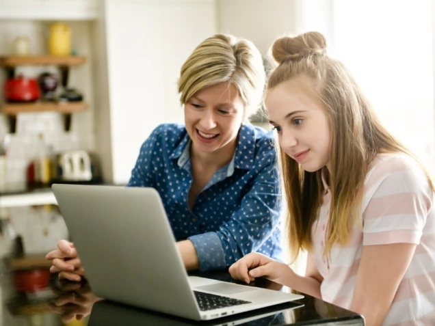 A mother using a laptop in kitchen with teenager